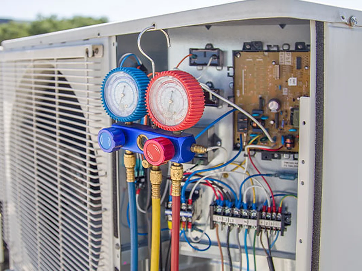 Refrigerant manifold gauges connected to a condensing unit with its control panel open