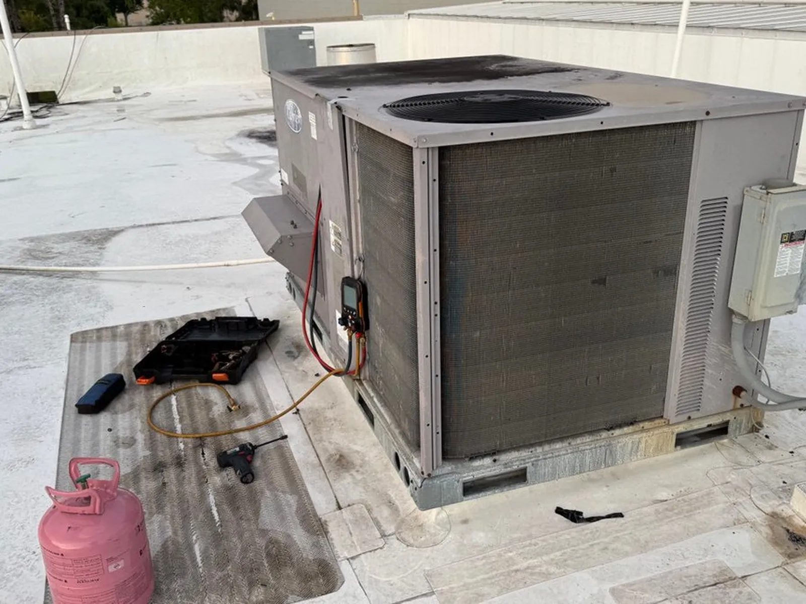 Rooftop package unit opened for service with tools and a refrigerant cylinder